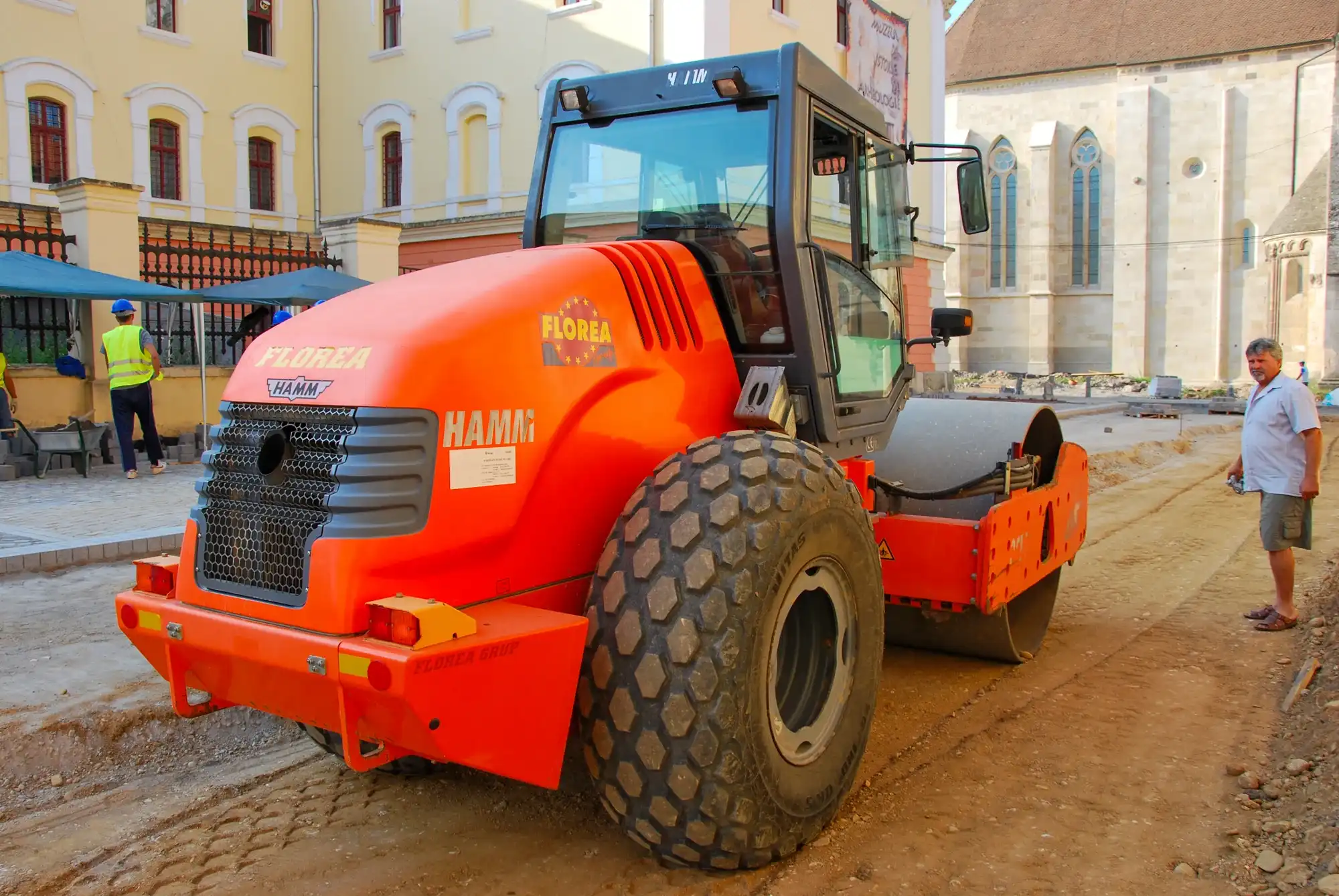 Cilindru compactor HAMM pe un șantier de pavare, lângă clădiri istorice