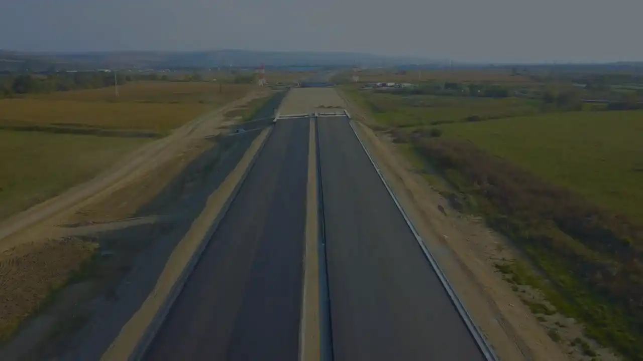 Vedere aeriană a unui drum nou asfaltat care traversează câmpuri, în Transilvania