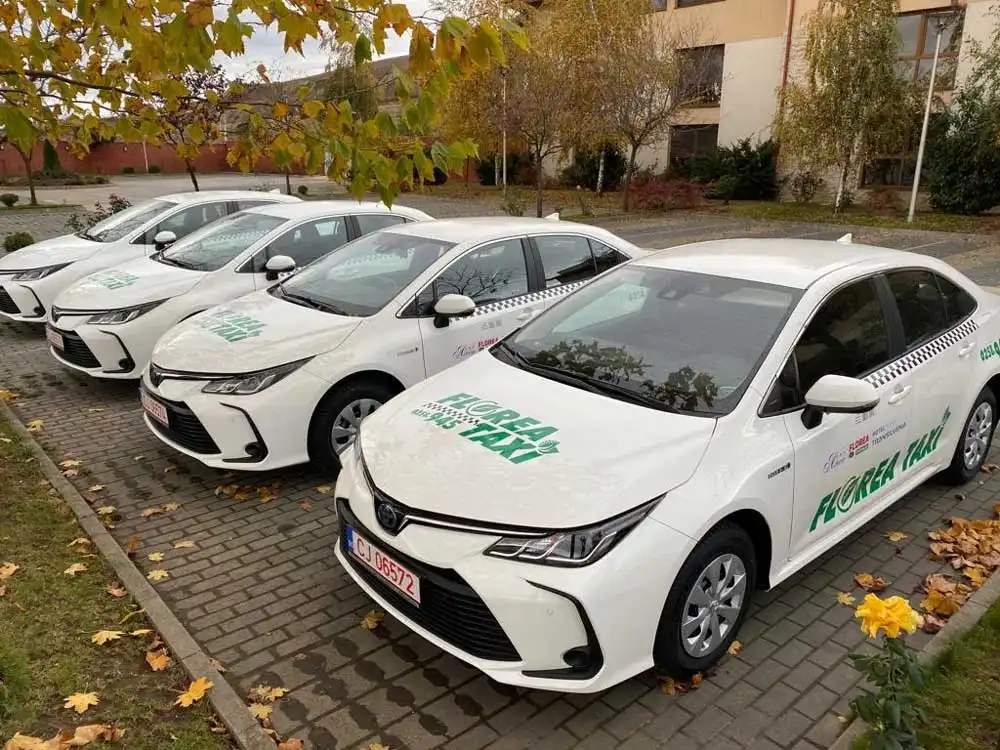 Autoturisme hibride albe Florea Taxi, cu logo verde, parcate în rând
