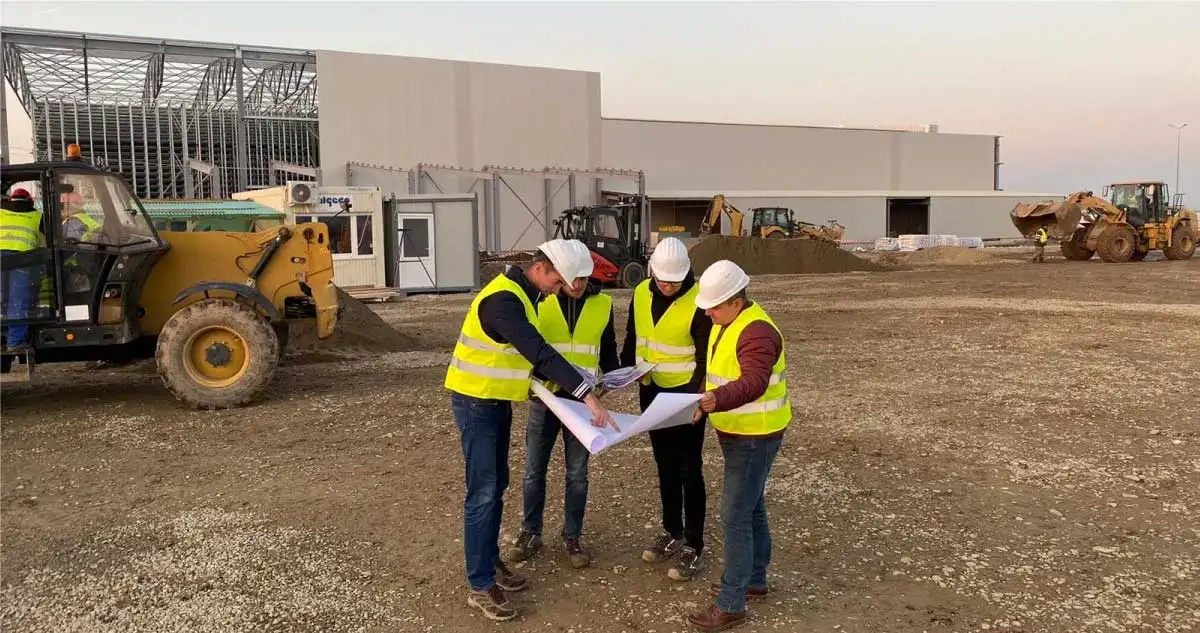 Ingineri cu căști de protecție analizând planurile pe un șantier industrial